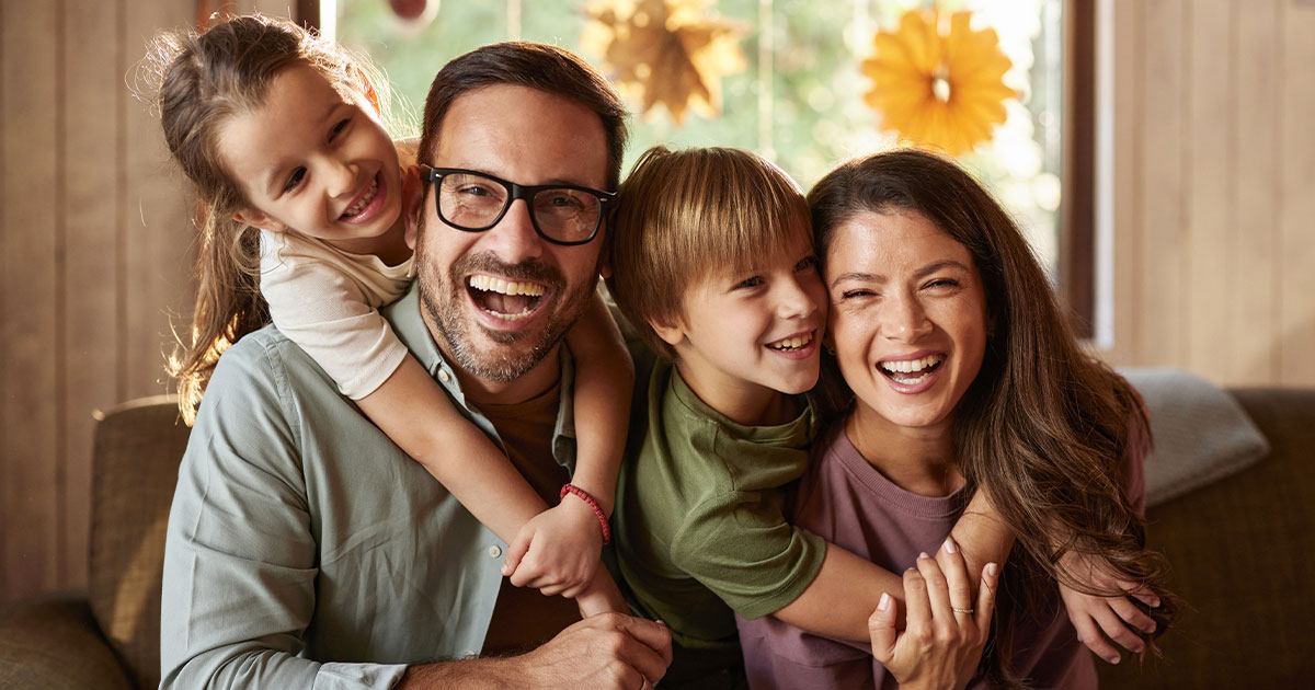Ein vierköpfige Familie sitzt auf der Couch und lacht in die Kamera als Symbol für die B.A.S.I.S.-Methode.