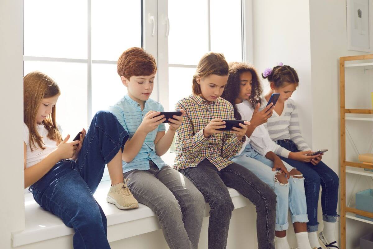 Fünf Kinder sitzen mit dem Smartphone auf dem Fensterbrett als Bild für den Medienkonsum von Kindern.
