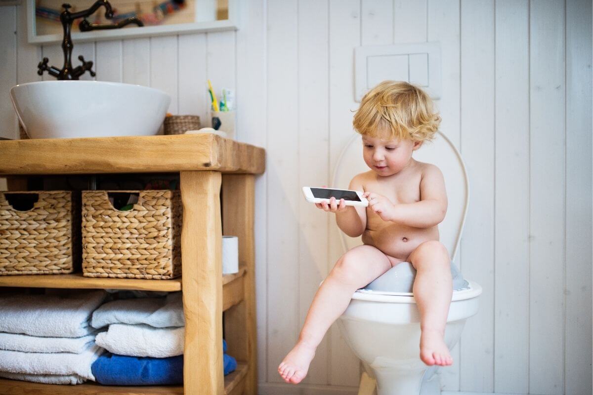 Ein Kind sitzt allein auf der Toilette und schaut in das Smartphone. Als Bild für den Medienkonsum bei Kindern im Vorschulalter