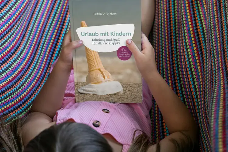 Ein Mädchen hält das Buch "Urlaub mit Kindern" von Gabriele Reichart.