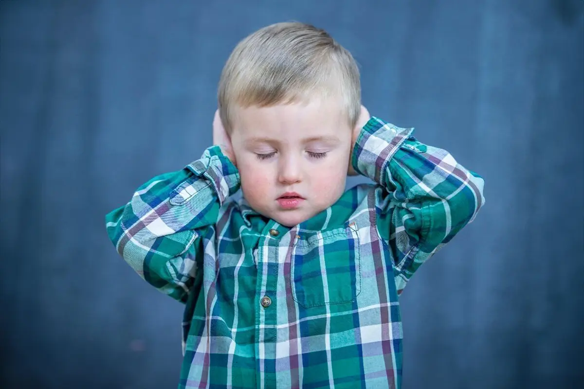 Ein ca. vierjähriger Junge hält sich die Ohren zu und schließt die Augen