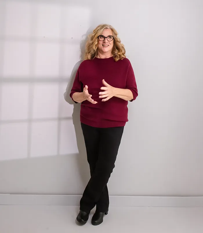 Gabriele Reichart, Dipl. Sozialpädagogin und Erzieherin, zeigt den Weg ins Familienglück. Sie lehnt im roten Sweater entspannt an einer Wand und schaut in die Ferne.