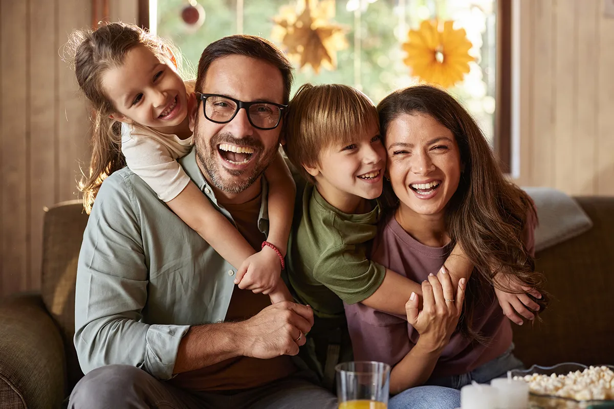 Ein vierköpfige Familie sitzt auf der Couch und lacht in die Kamera als Symbol für die B.A.S.I.S.-Methode.