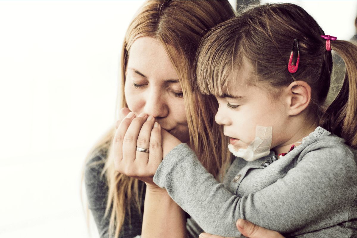 Mutter gibt einem kleinen Mädchen ein Küsschen auf eine Verletzung an der Hand